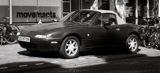 A black and white Mazda MX-5 parked between bicycles in Haarlem