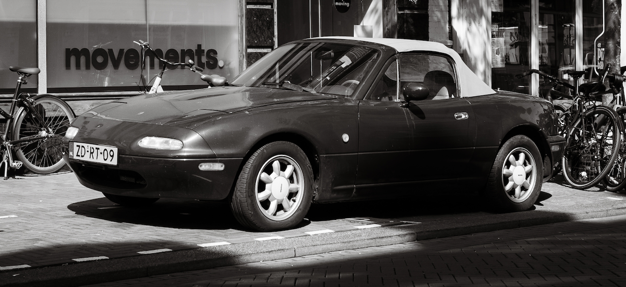 A black and white Mazda MX-5 parked between bicycles in Haarlem