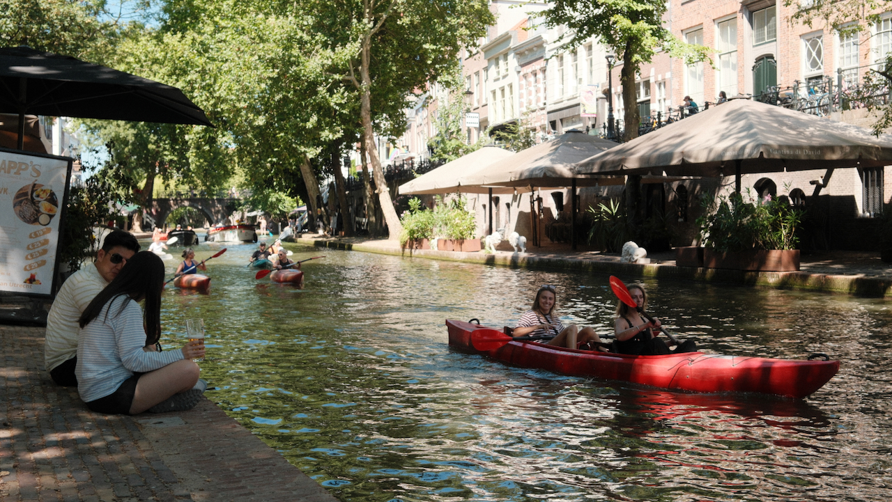 Two women paddling a red kayak along an Utrecht canal