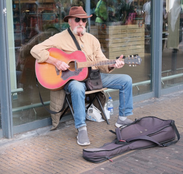 A street musician playing a red acoustic guitar in Zaandam