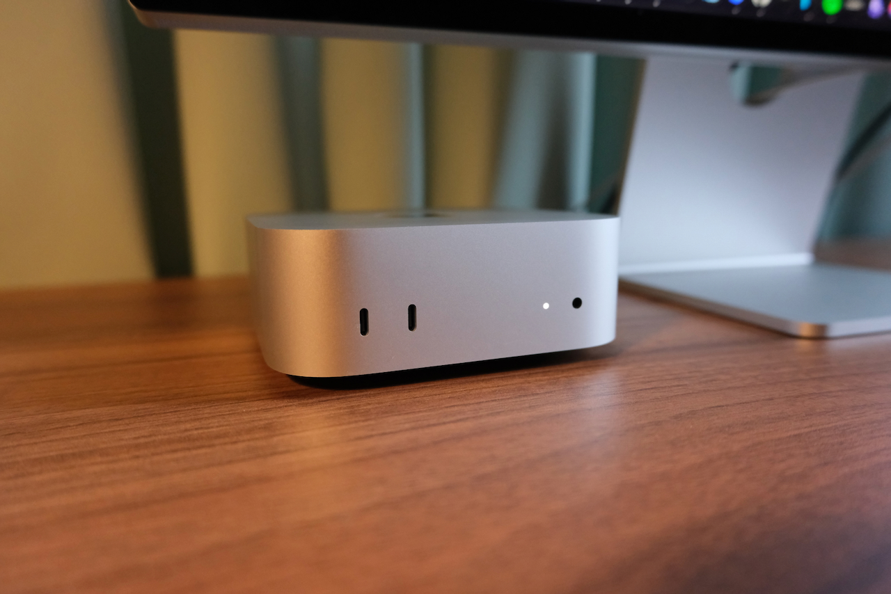 A Mac mini on a wooden desk beneath a monitor